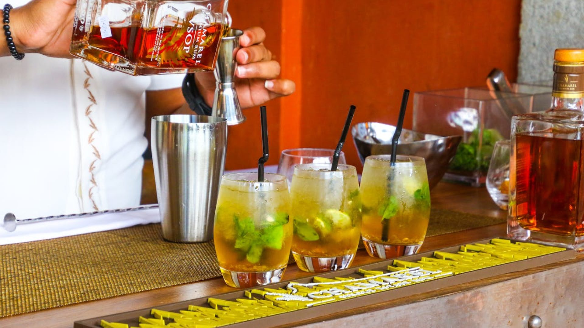 A picture of a bartender in a cocktail masterclass making 3 sets of cocktails with his shaker, jigger and a bottle of whiskey.